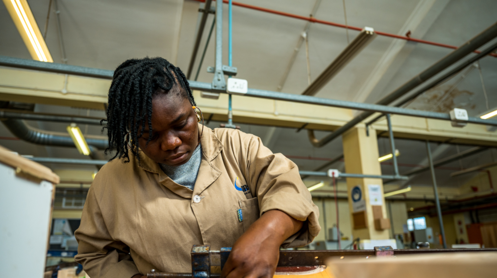 A woman in a brown shirt works with tools in a factory