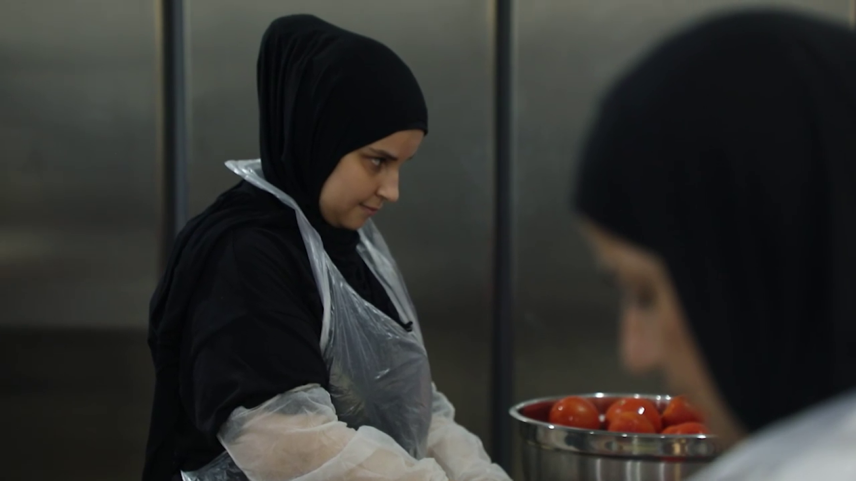 A woman in a black head wrap puts gloves on in the kitchen and puts gloves on.