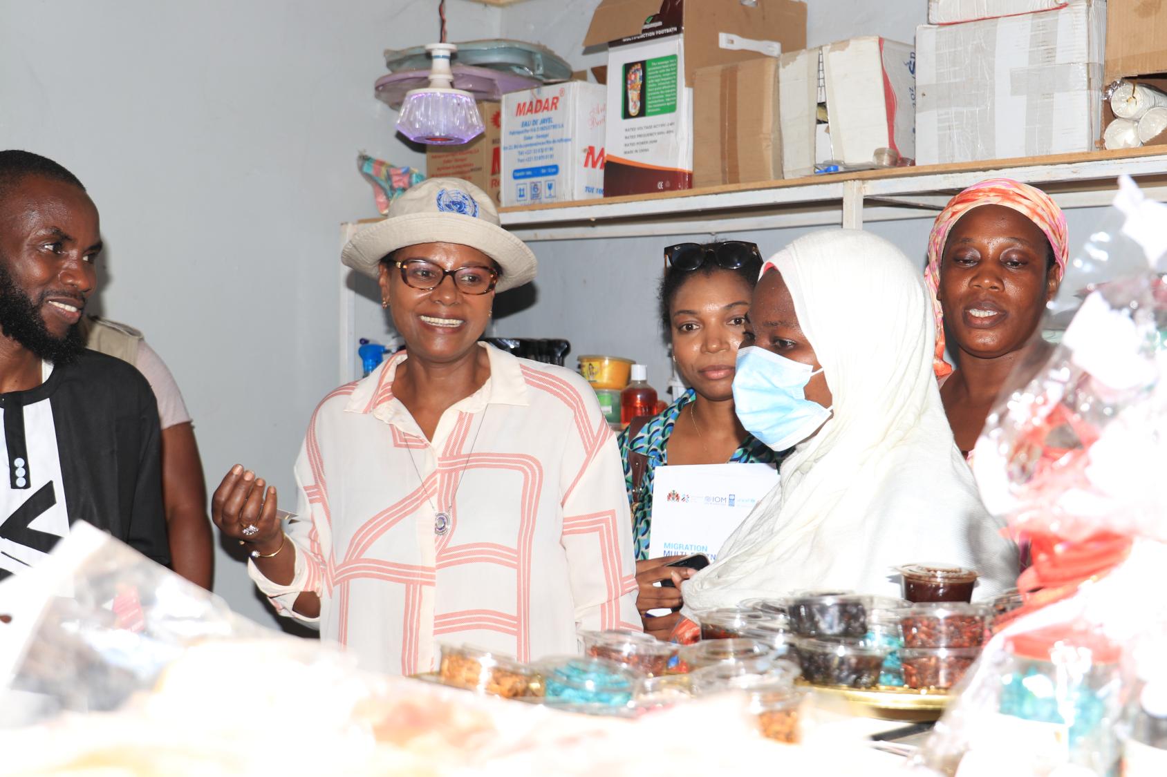 A woman in a peach shirt with a hat talks to customers in a shop