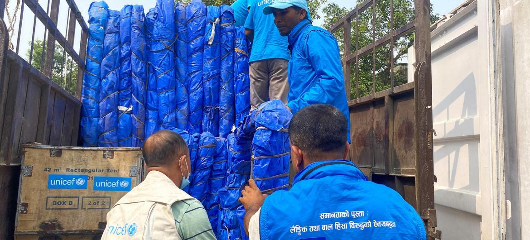 People unload trucks with humanitarian supplies, wearing blue vests.