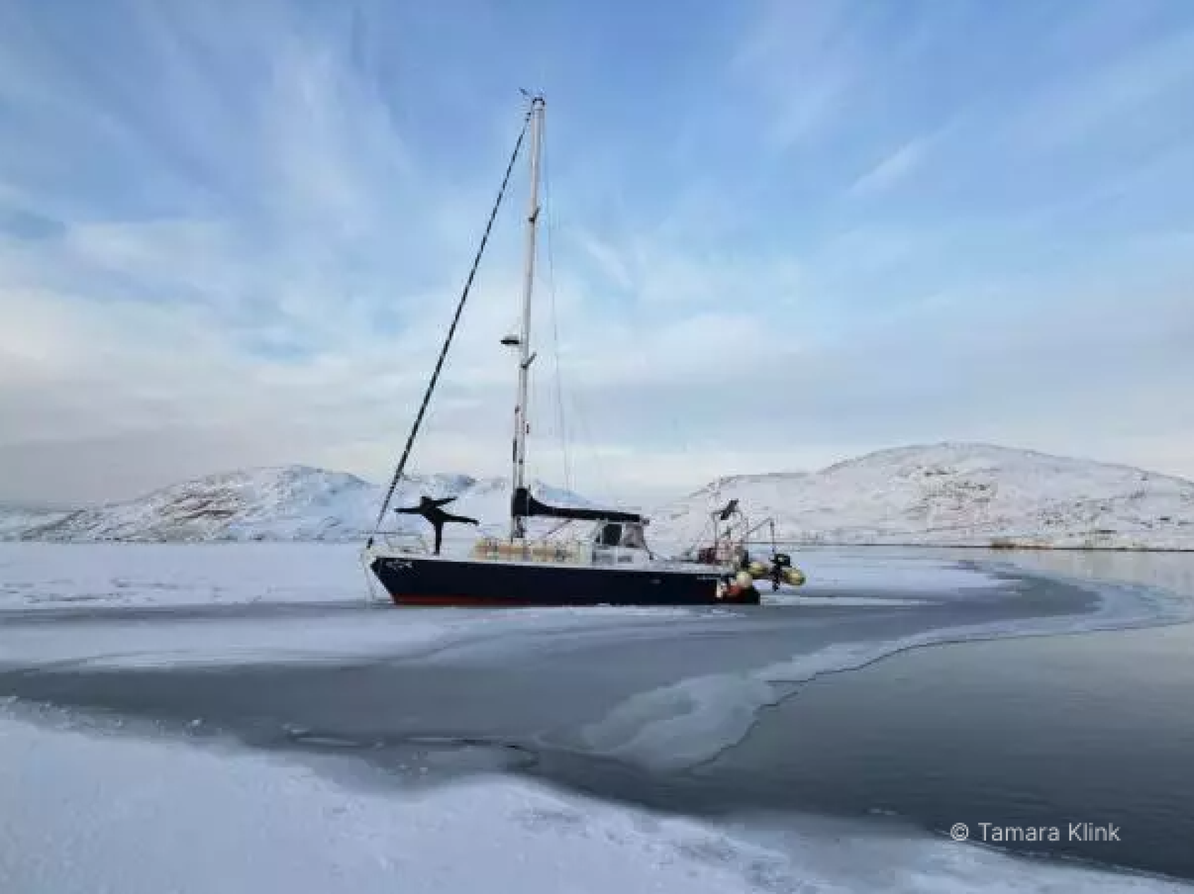 A ship on ice and water, with mountains in the distance.