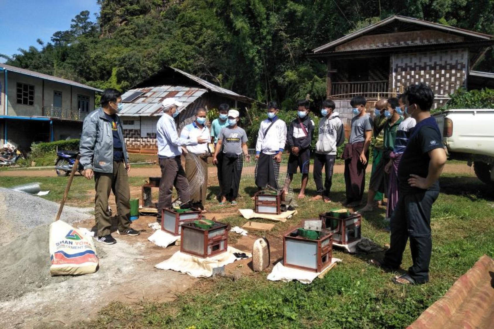 A group of men stand in front of houses, examining a row of metallic stoves