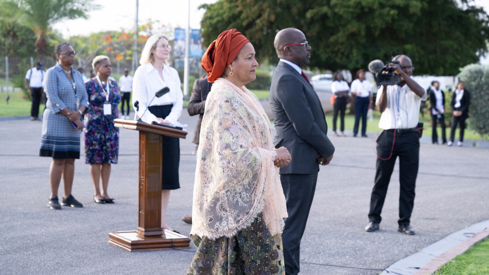 The image features a group of individuals at an outdoor event. In the foreground, there is the DSG and PM, facing away from the camera.