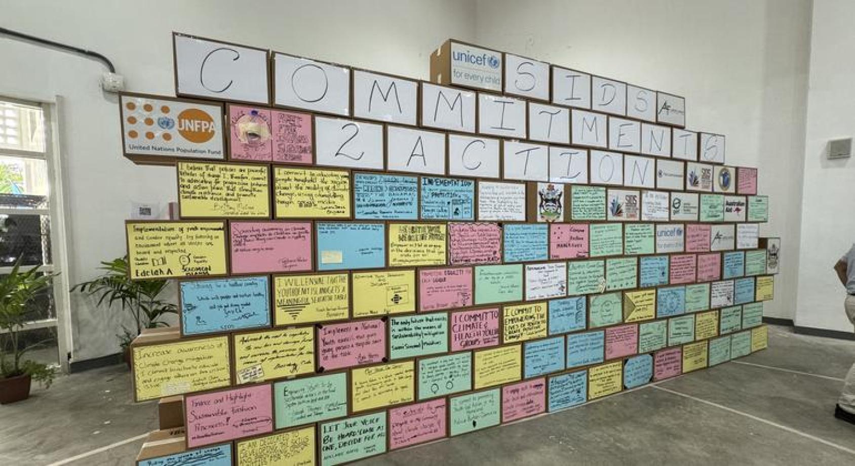 Стена с коробками, на которых наклеены листки с надписями от руки и заявлением, что островные государства обязались действовать