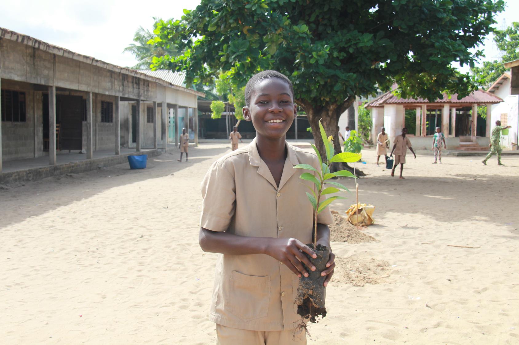 Un petit garçon tenant une plante et souriant à la caméra.