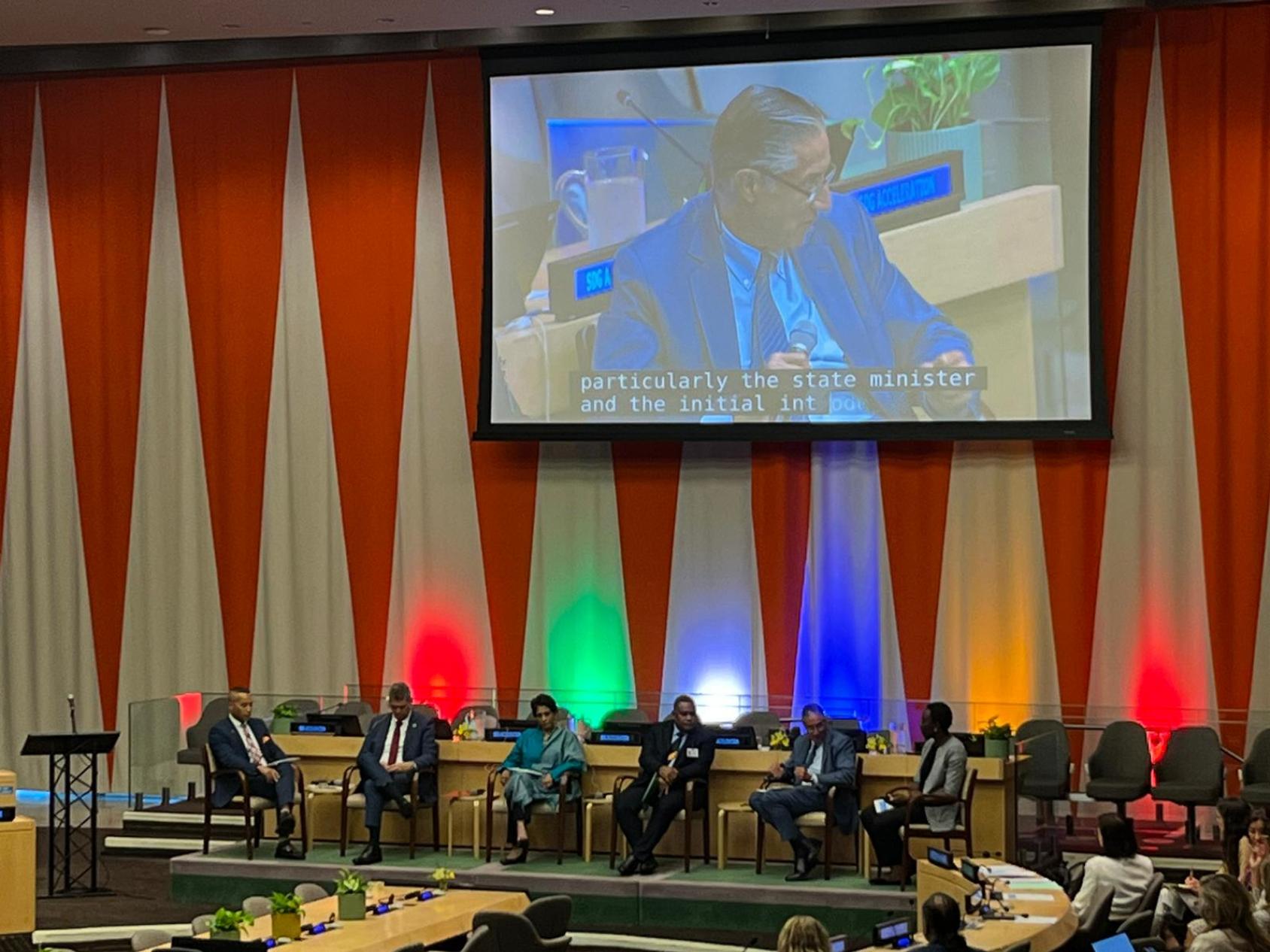 A group of people seated in front of a podium where there is a projection of one of the speakers