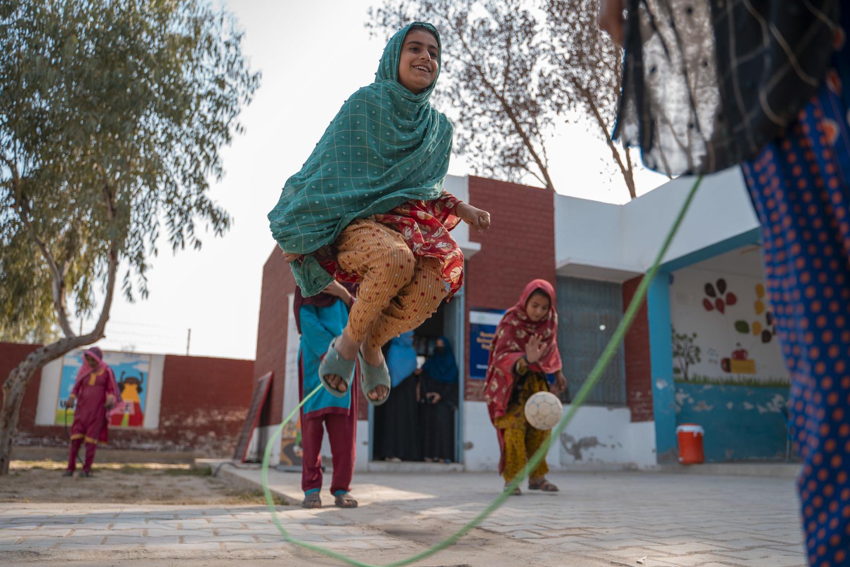 A group of girls in colourful clothes play jumprope, with smiles on their faces.