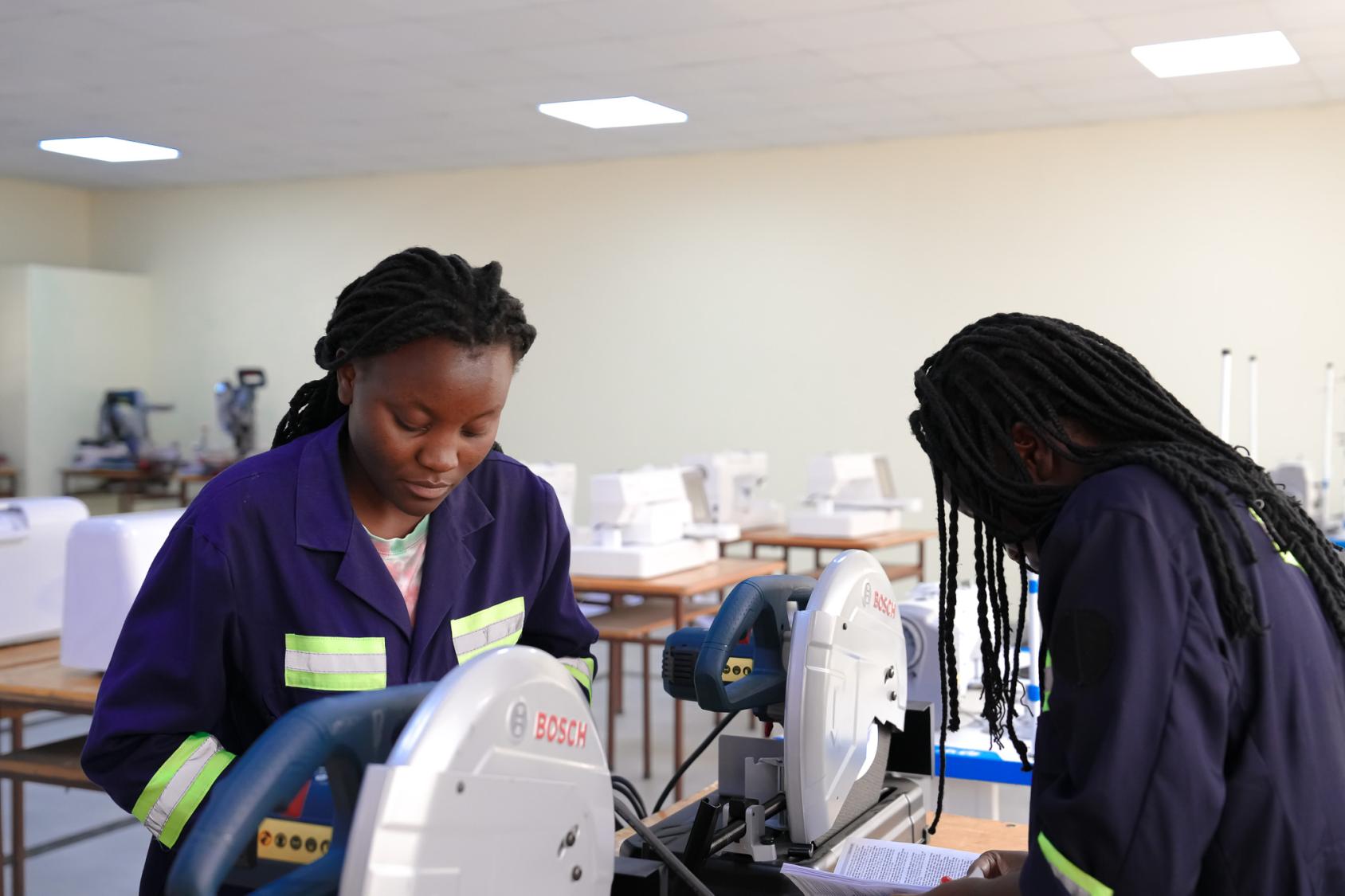 Two women in jumpsuits stand over a machine
