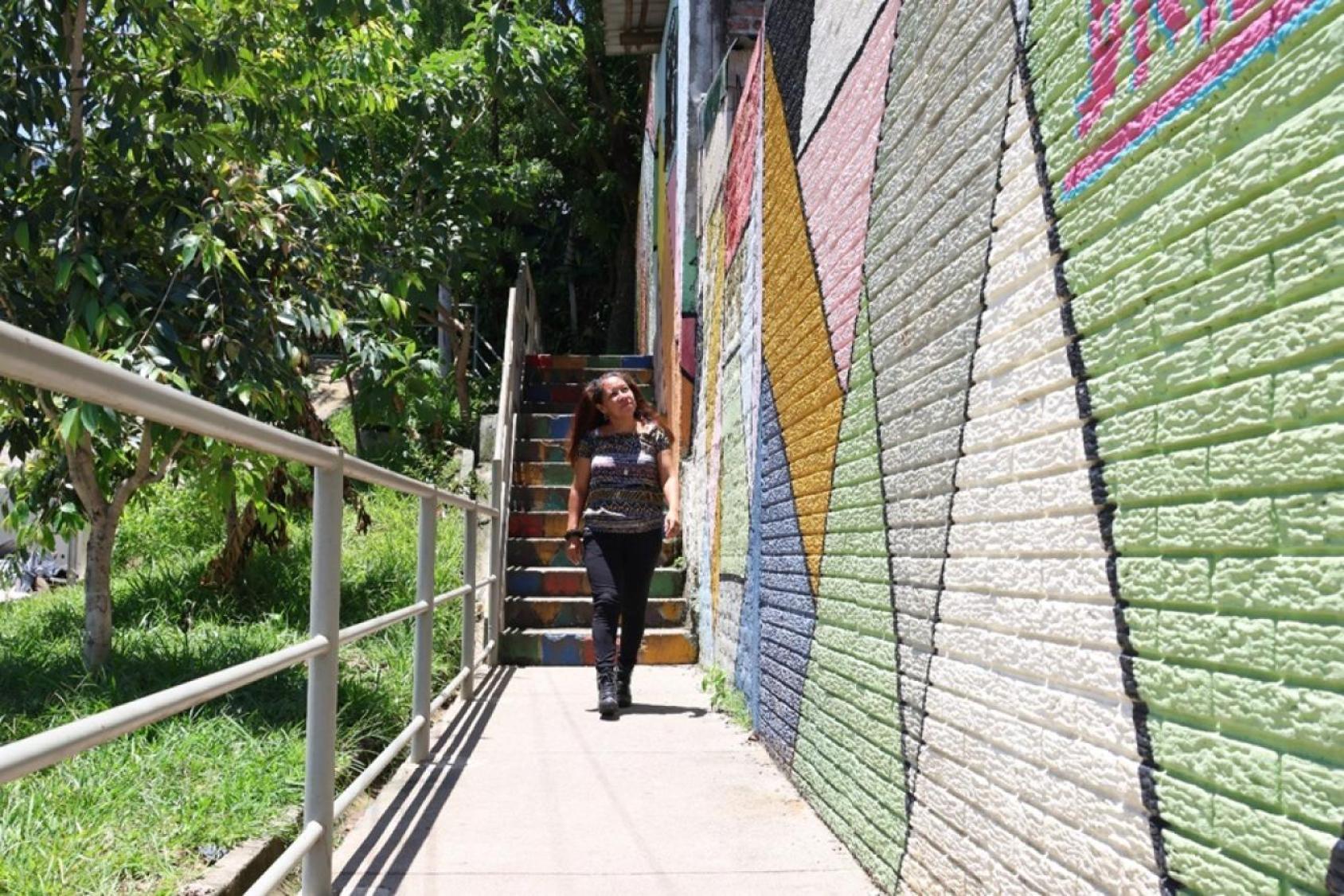 A woman in a black uniform walks down a flight of stairs against a colourful wall