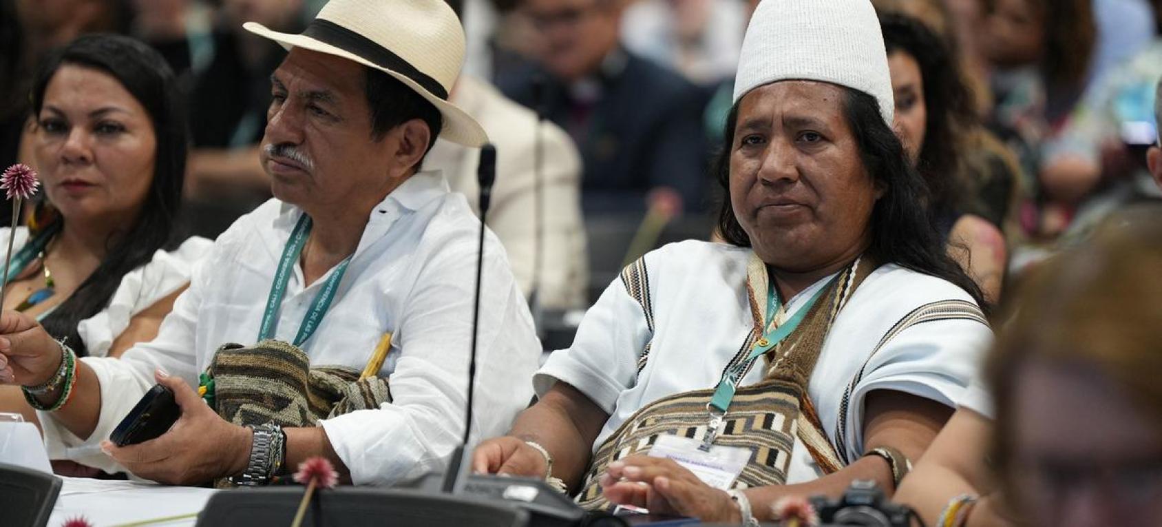 A row of three people in traditional indigenous clothing listen to proceedings