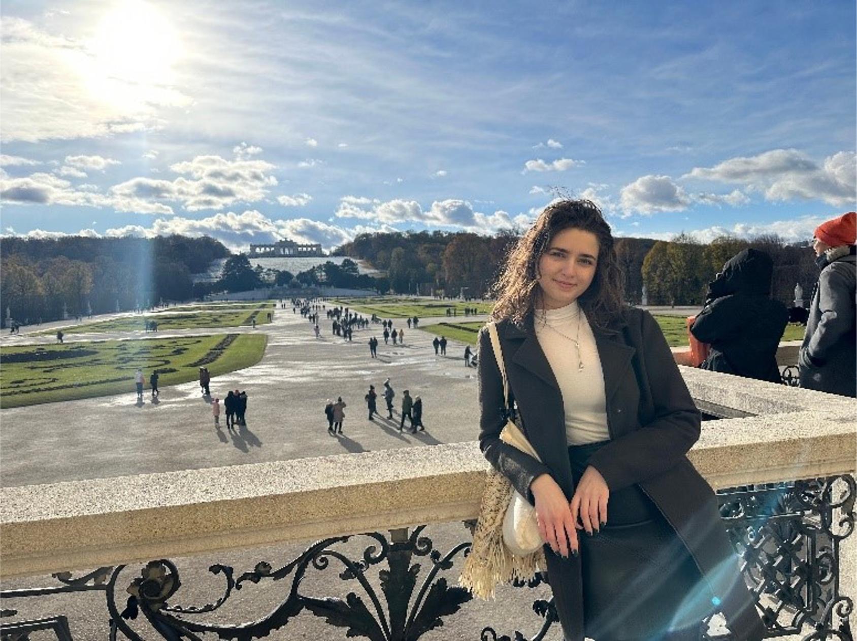 A picture of a girl in a black blazer as she leans against a parapet in a university building.