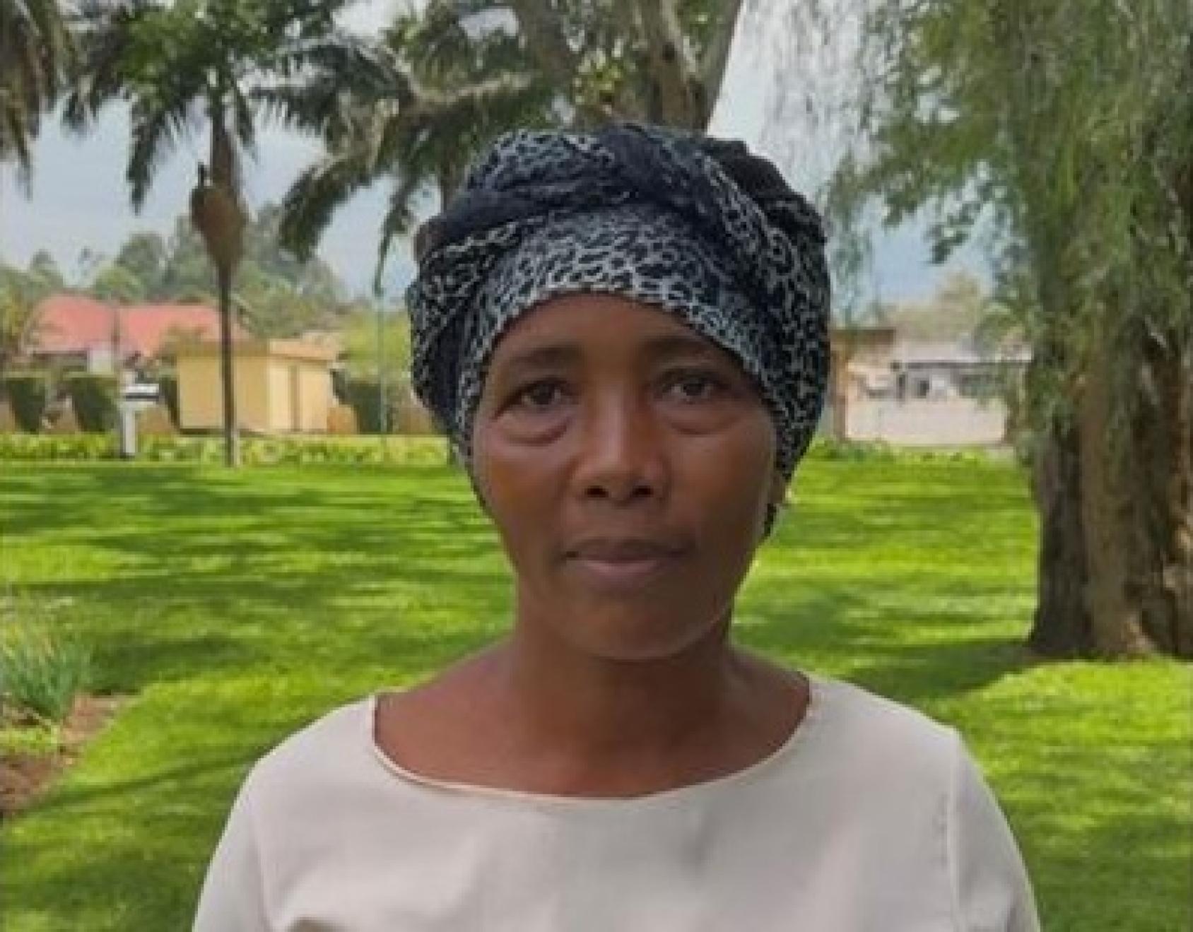 A woman stands in front of some trees and grass.
