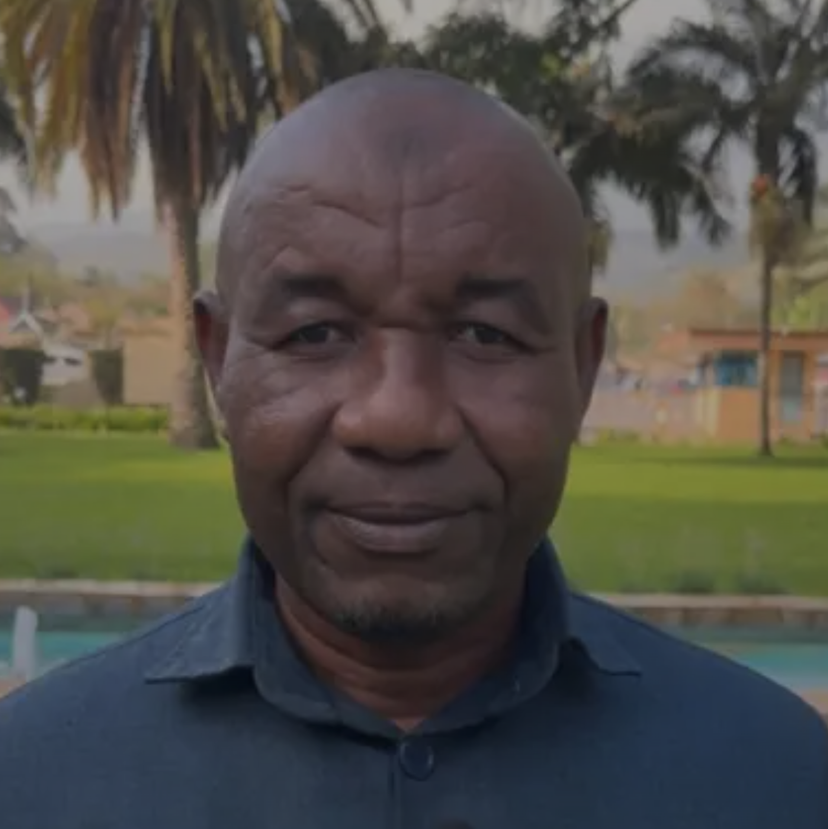 A man stands in front of some buildings surrounded by grass and trees.
