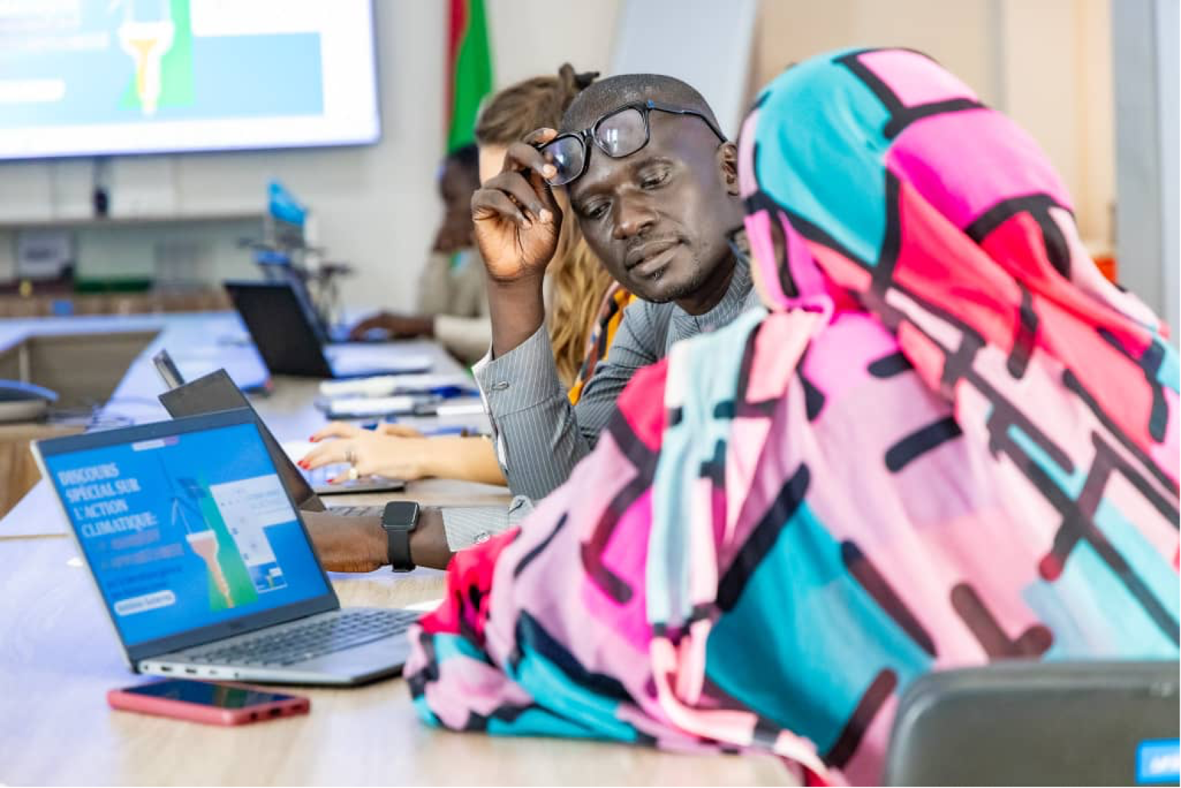 A woman is speaking to a man and looking at a screen