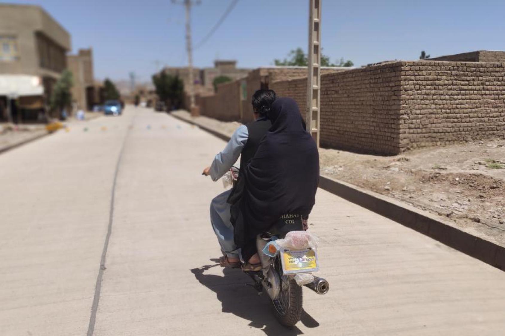 امرأة تُنقل على دراجة نارية على طريق خرساني مُعاد تأهيله في قرية سيد آباد، مدينة هرات – ١١ مايو ٢٠٢٥