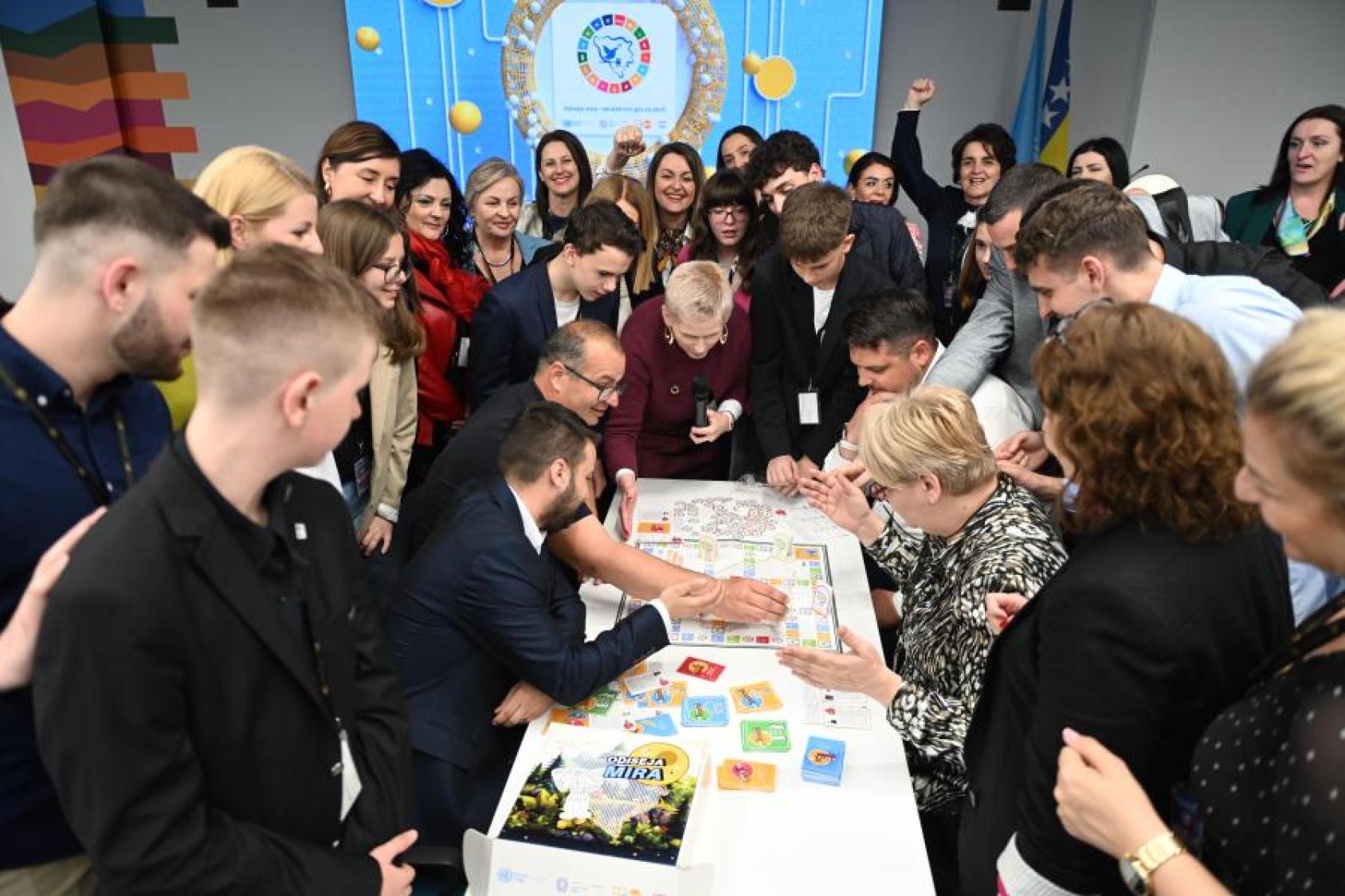 A group of young and older people gather around a boardgame in excitement