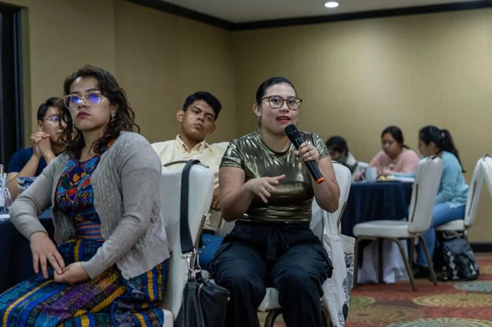 A young woman speaks into a microphone at a meeting