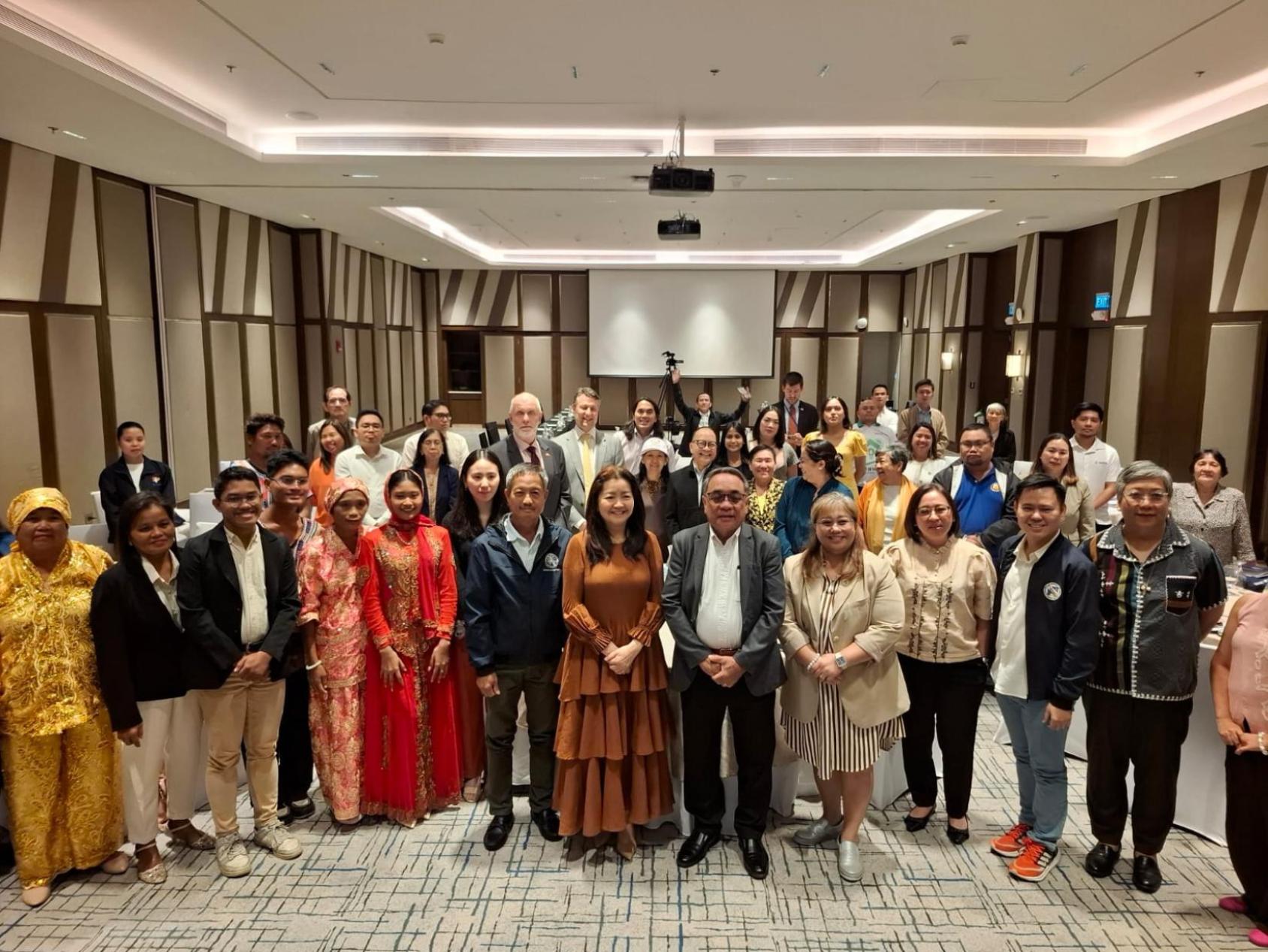 A group of men and women in colourful clothes stand in a formal room