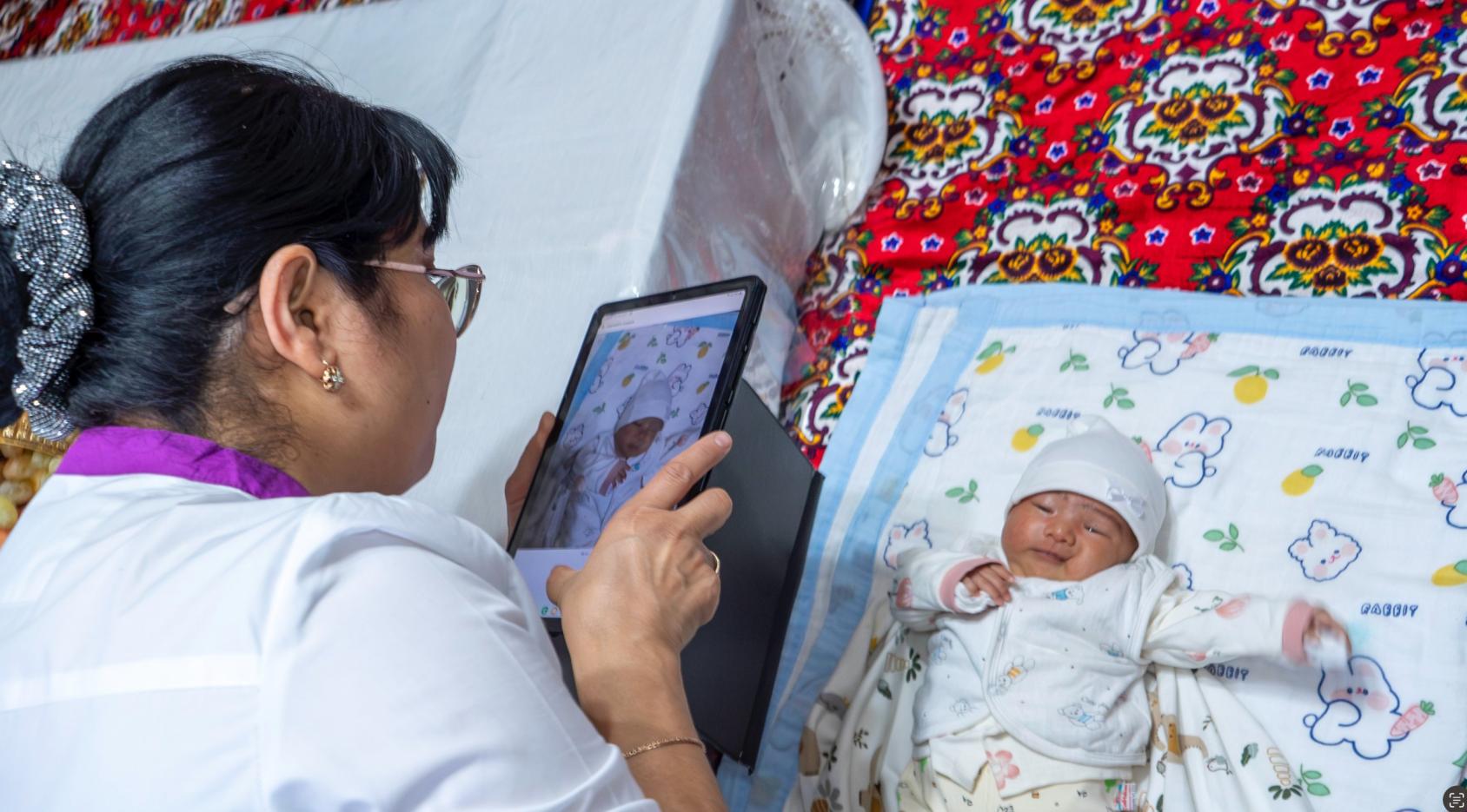 A nurse in a white uniform takes a picture of a baby swaddled, using an electronic tablet