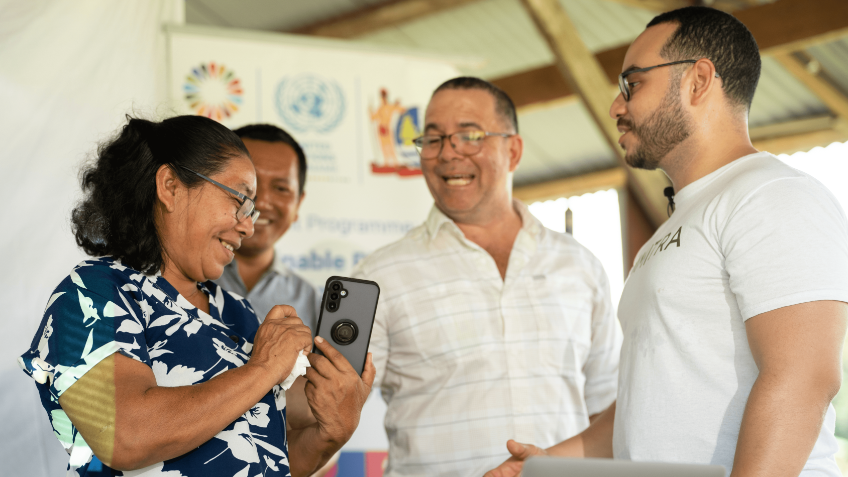 A woman shows something on her mobile phone to another woman as two men look on.