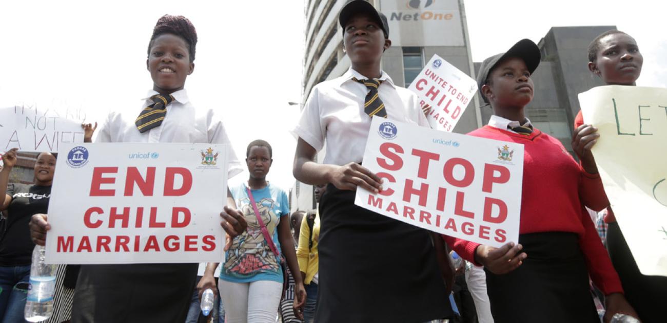 Plusieurs jeunes filles vêtues d’un uniforme scolaire protestent dans la rue. Elles tiennent entre les mains des pancartes sur lesquelles est écrit, en rouge, « Stop child marriages », qui signifie en français « Stop aux mariages d’enfants ».