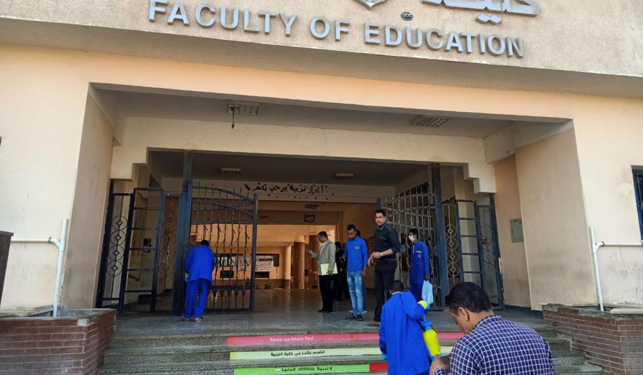 Shows men in protective gear cleaning the steps of the Faculty of Education.