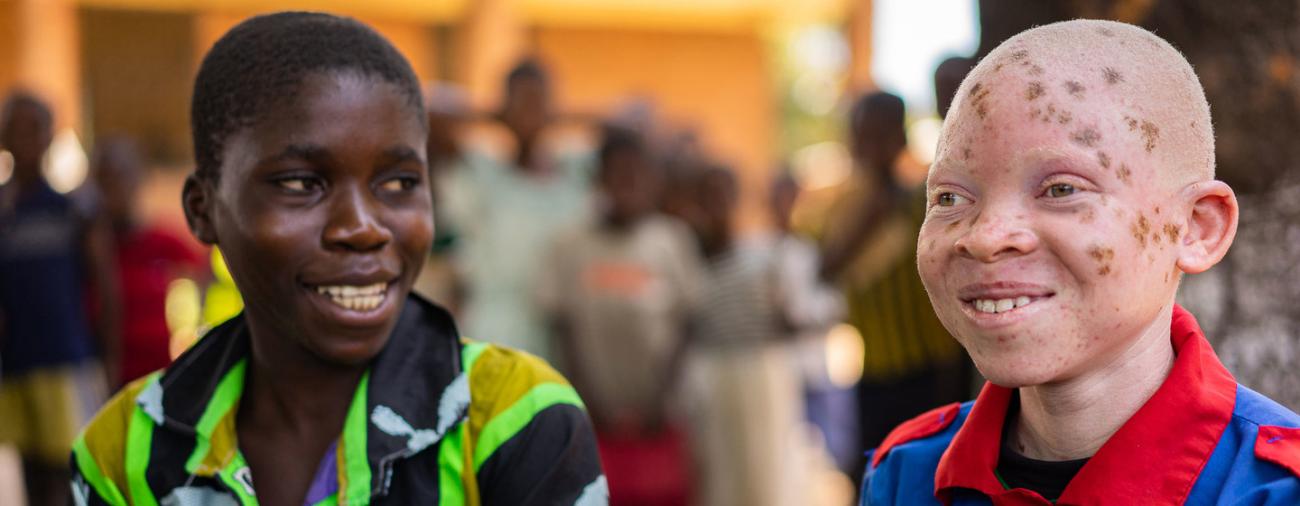 患有白化病的孩子钦西-贾法利（右）与他的同学（左）坐在一起，面带笑容。