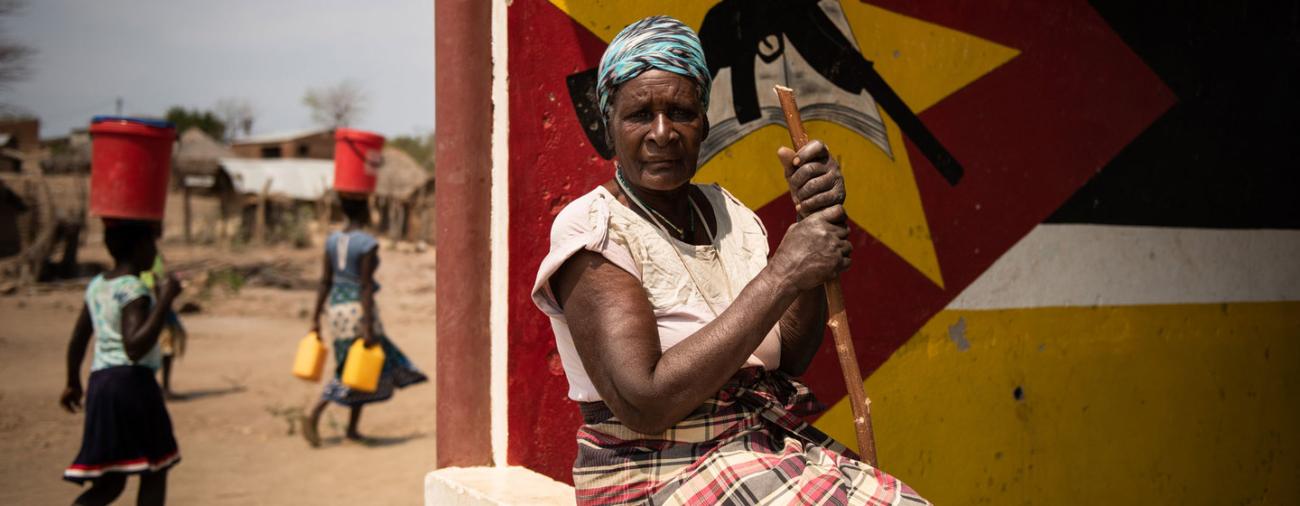 امرأة فرت من الصراع تقف أمام جدار مصبوغ وتحدق إلى الأمام بثبات.