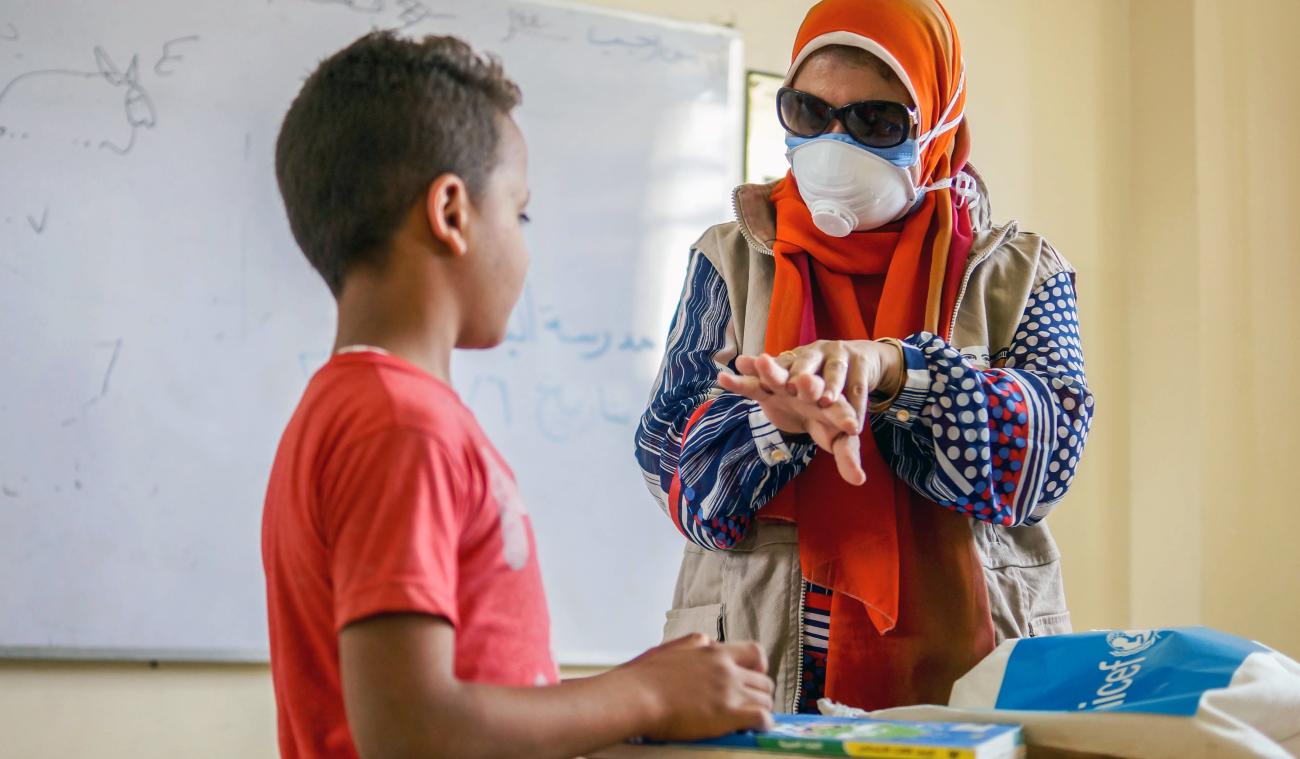 Un membre féminin du personnel de l'ONU portant un masque de protection donne à un jeune garçon des conseils de sécurité en lui montrant les gestes appropriés à faire pour un lavage efficace des mains.