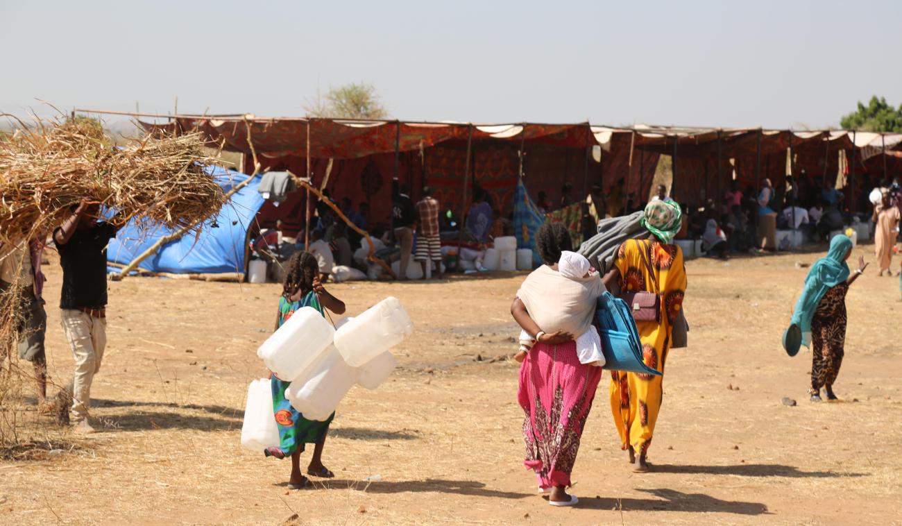 Refugees and migrants carry jugs and supplies near the camp.