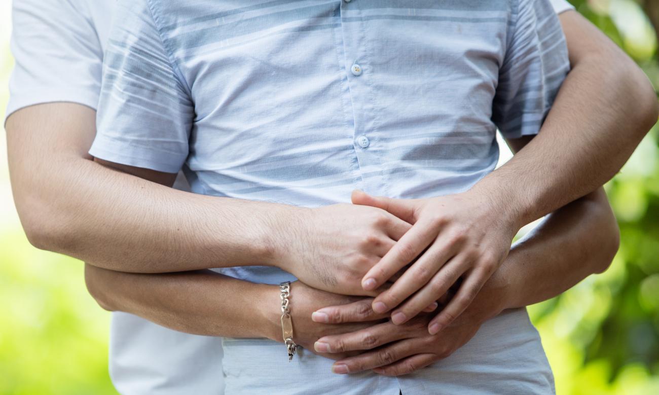 Foto del torso de dos hombres mientras uno abraza amorosamente al otro por detrás.