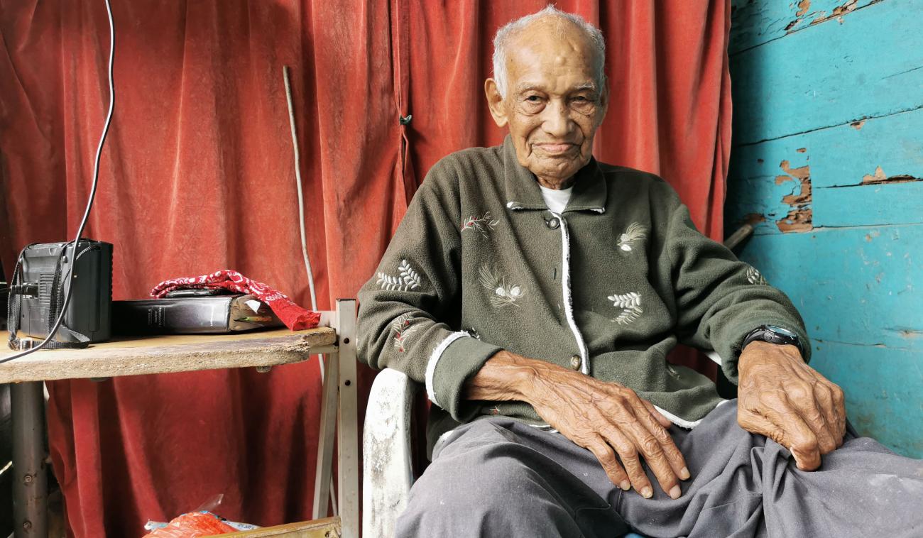 Candelario, un homme âgé, est assis près d'une table sur laquelle se trouve du matériel électronique. Il regarde la caméra en souriant.