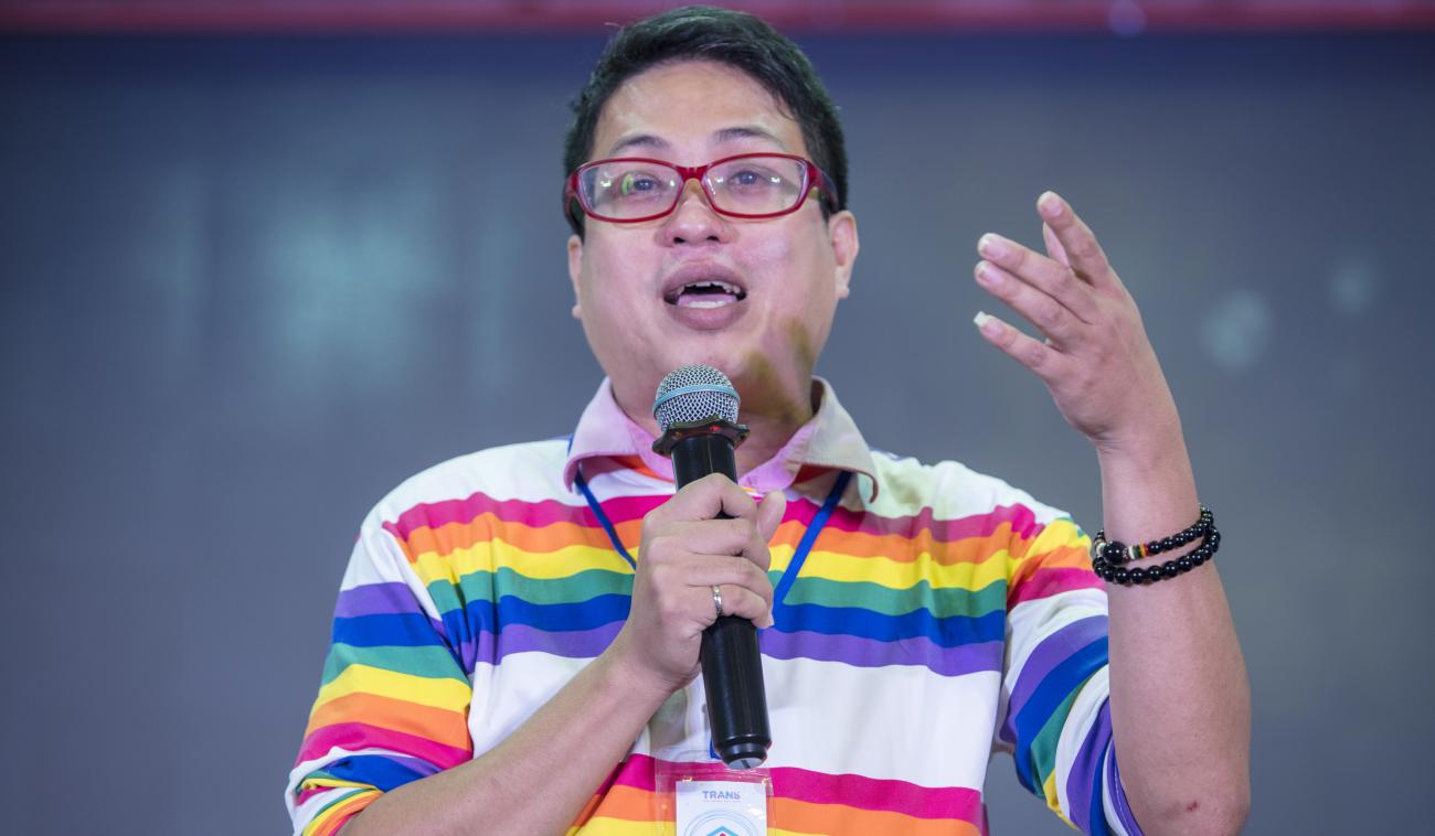 El Dr. Thu aparece hablando por un micrófono en el escenario de un evento.