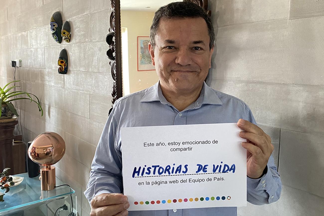 Un hombre sonríe dulcemente a la cámara mientras sostiene un pequeño letrero que comparte su visión de futuro sobre el sitio web, en español.