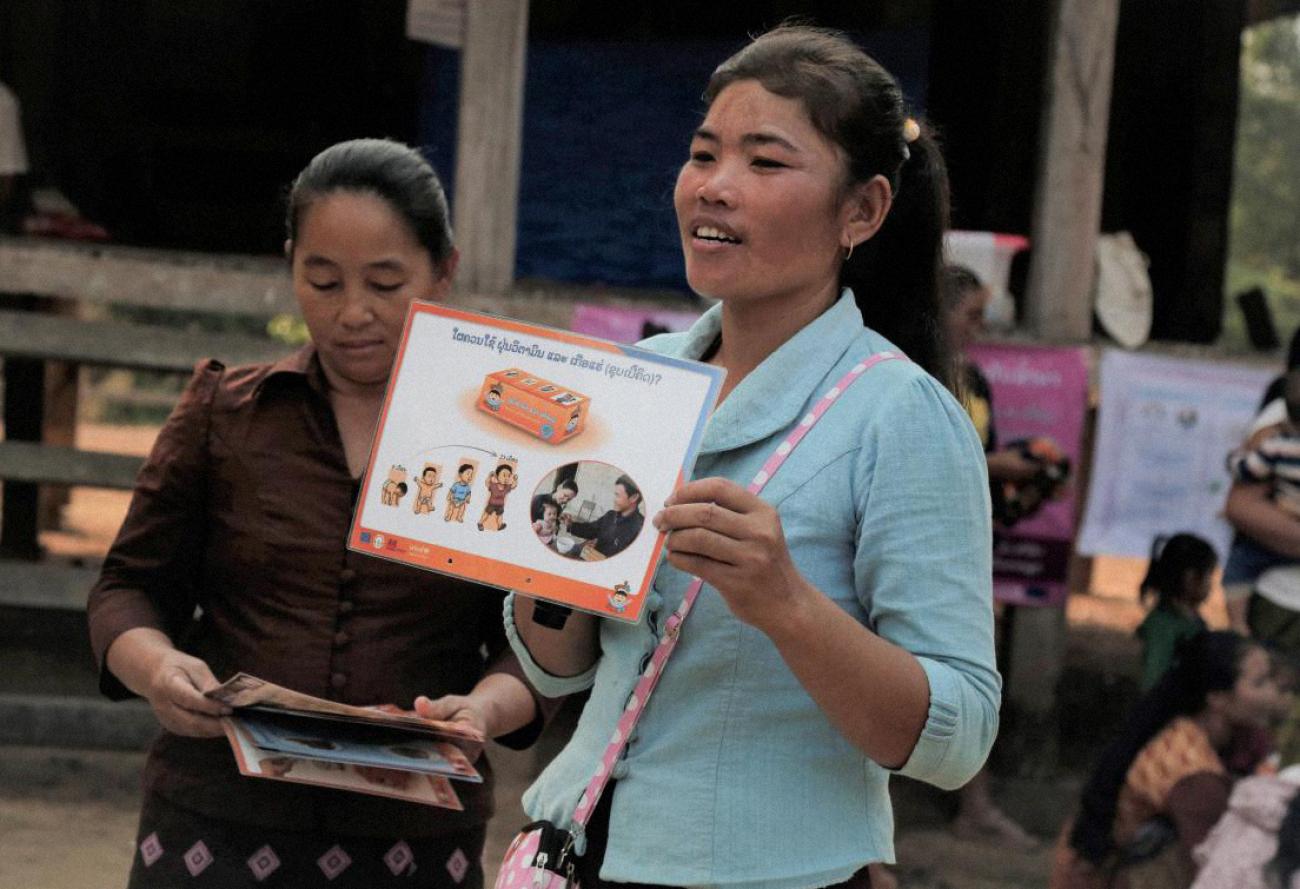 A woman in a blue shirt holds up a sign while another woman in a red shirt looks down at three other signs in her hands. 