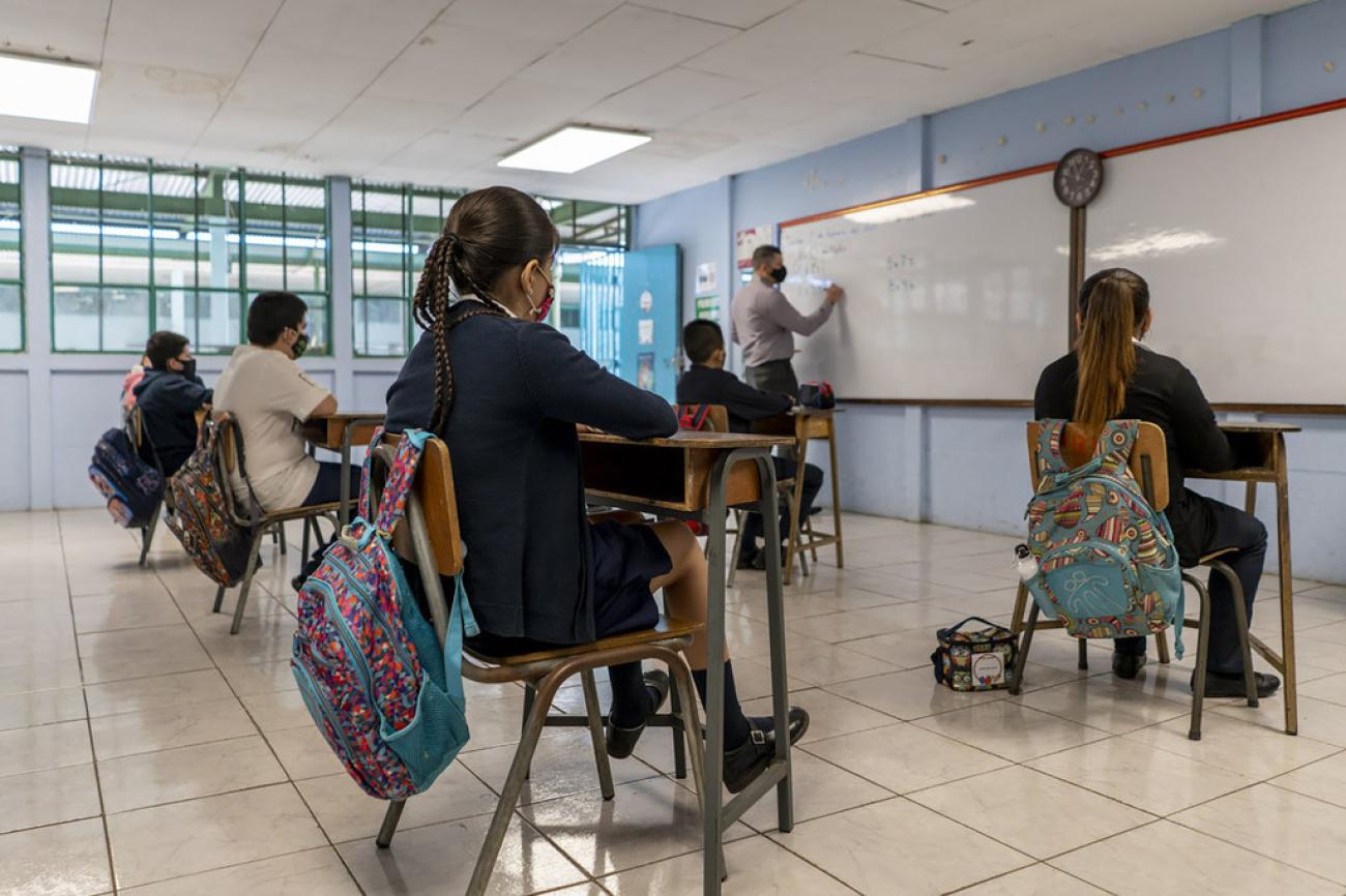 Children seated at desks attending in-person school at a social distance wearing masks. 
