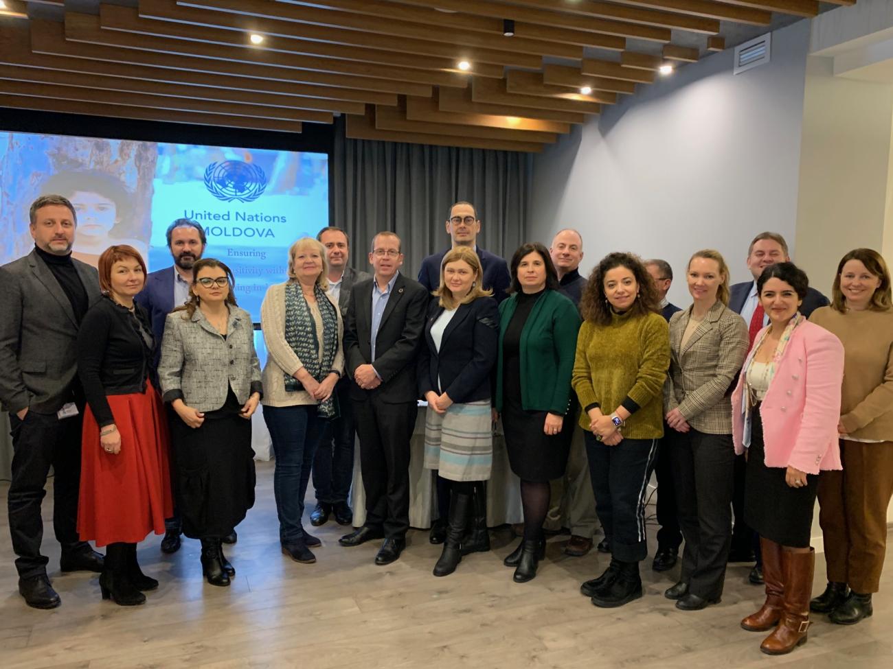 Un gran grupo de personas sonríe a la cámara frente a un proyector.