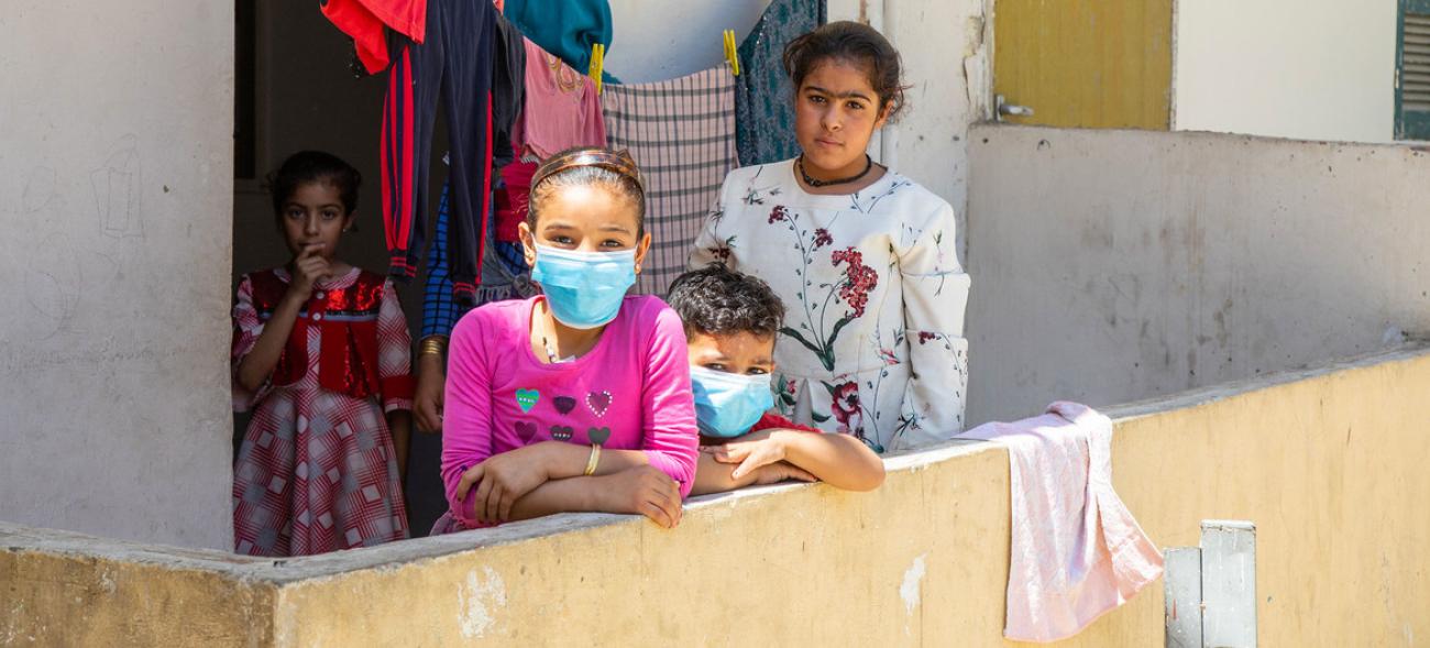 Four children stand in a balcony with drying laundry behind them. 