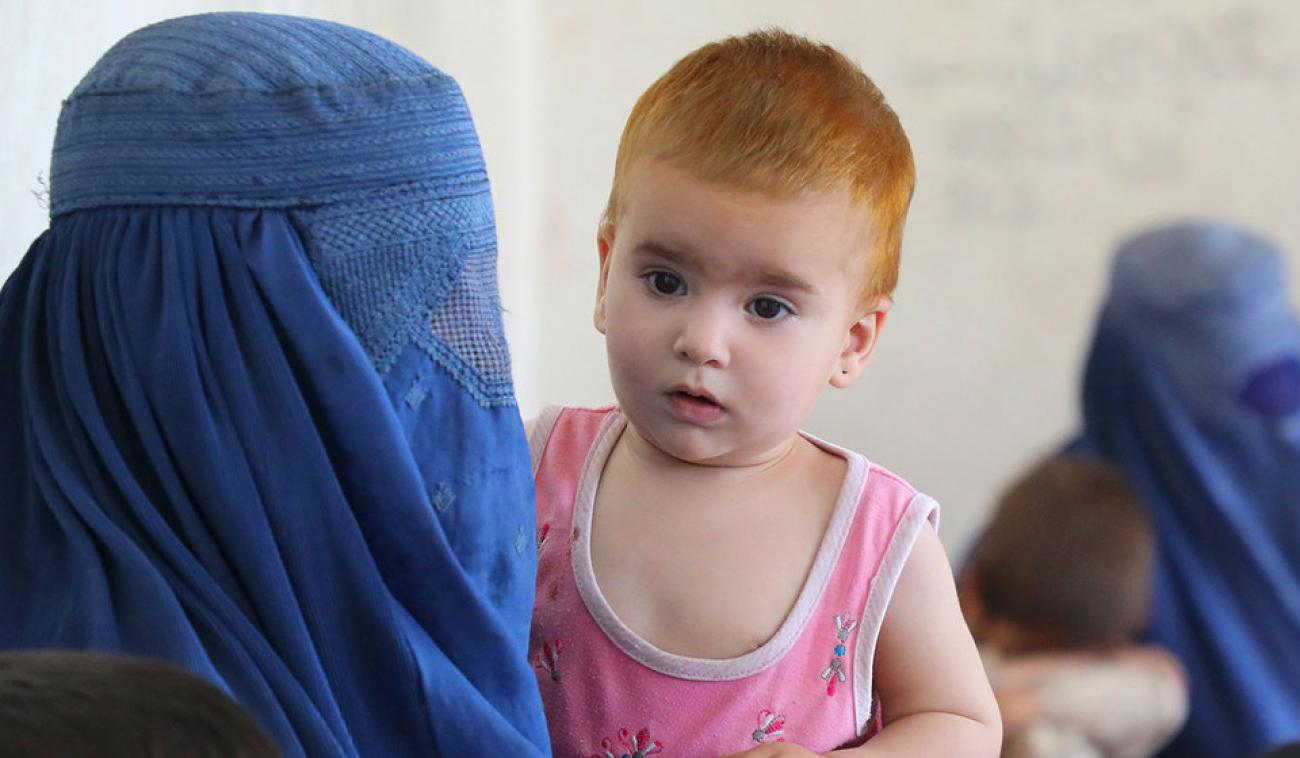最前面的一位母亲戴着头饰和脸，她抱着她的孩子，背景是另一位母亲和孩子。