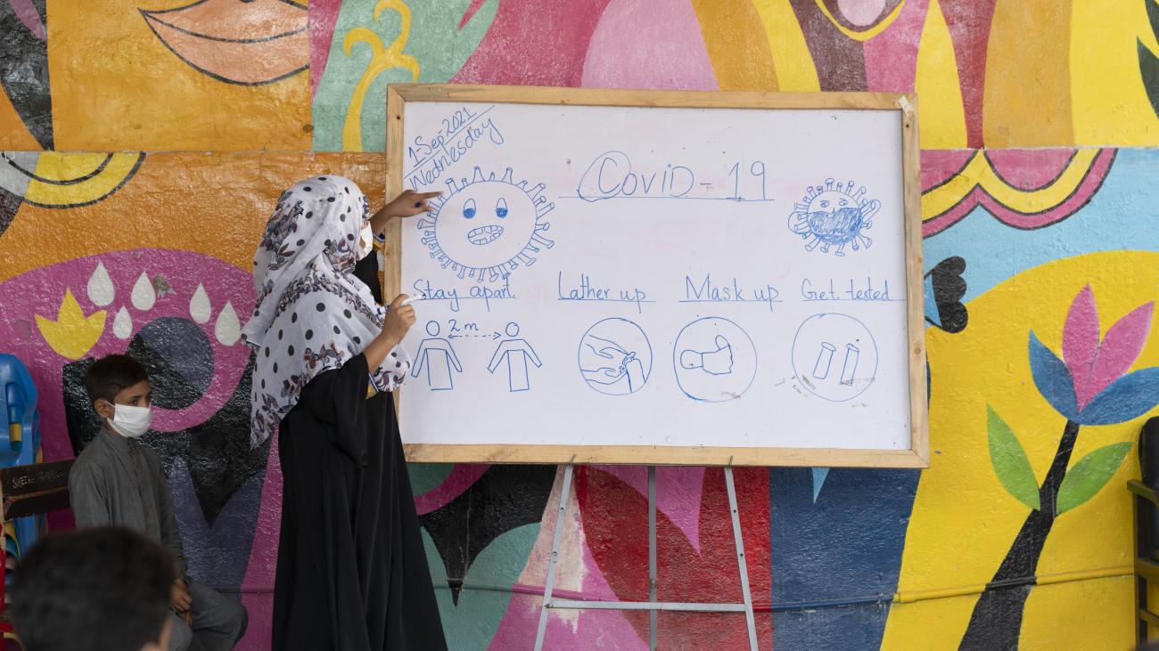 Una mujer señala una pizarra con información sobre los protocolos de seguridad relativos a la COVID-19. 