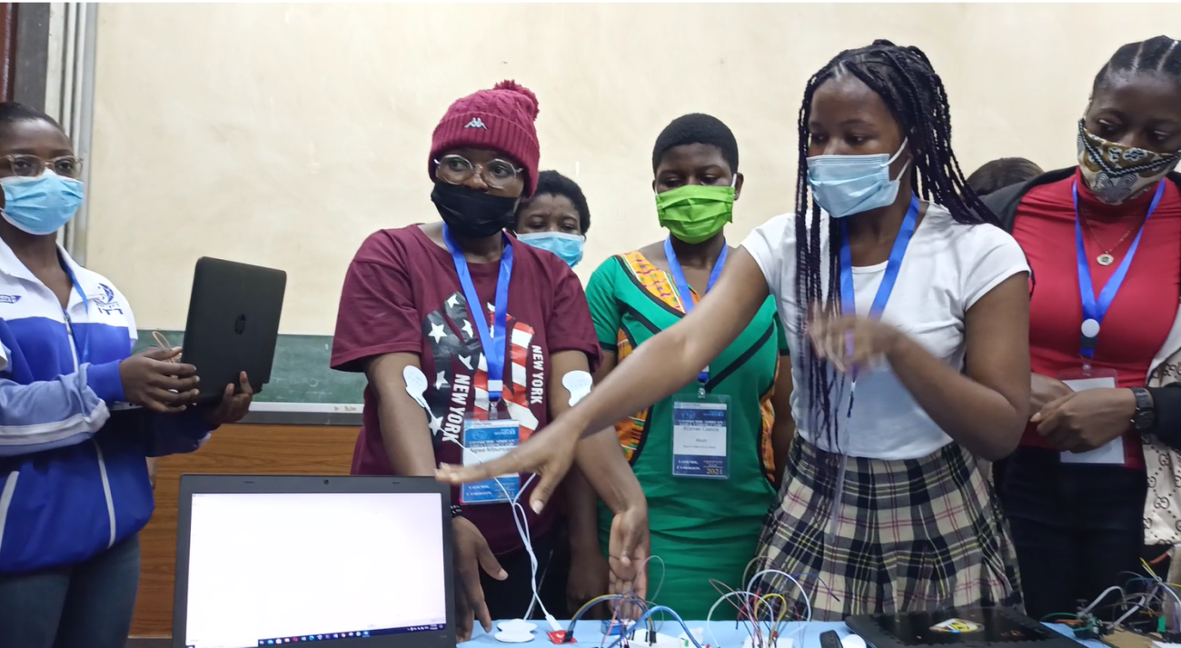 A group of young girls in masks point to computers. 