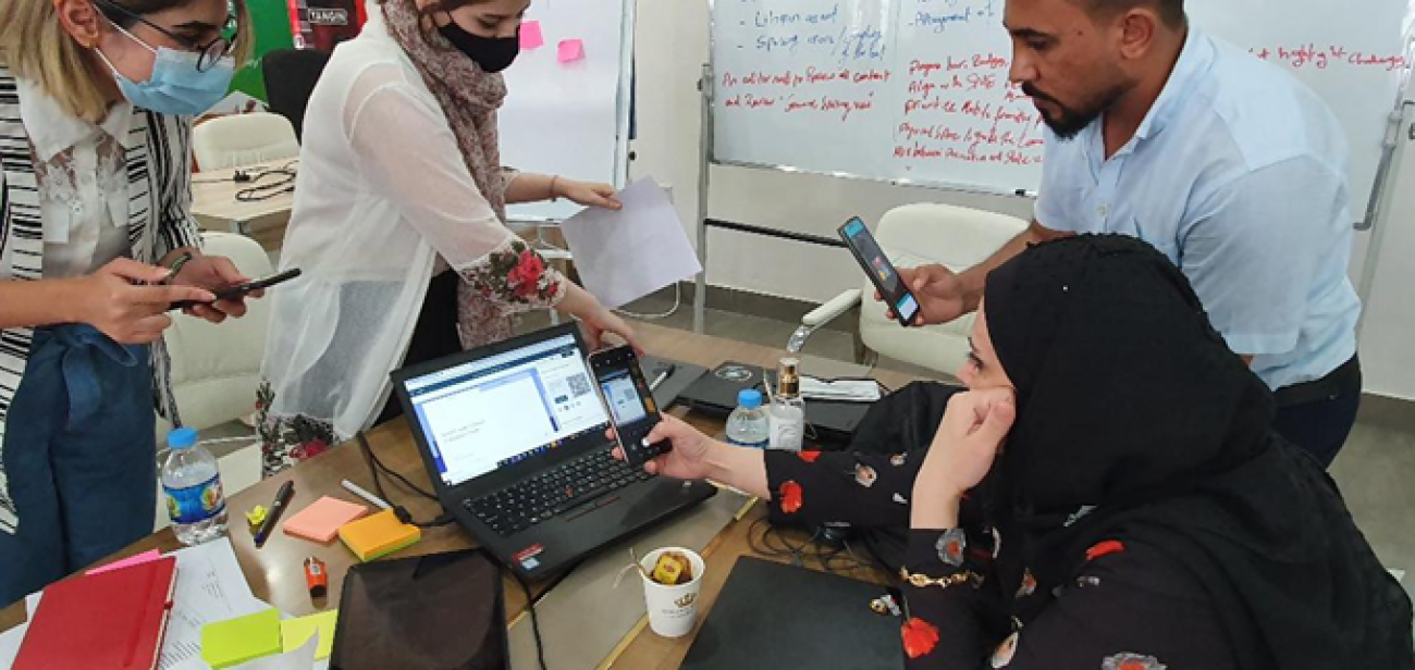 四人围在一台笔记本电脑旁工作。