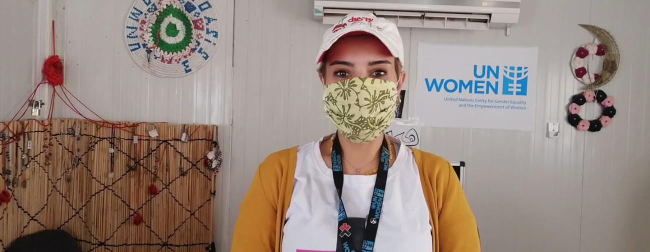 一名戴着口罩的妇女在联合国妇女署的标志旁直视着镜头。