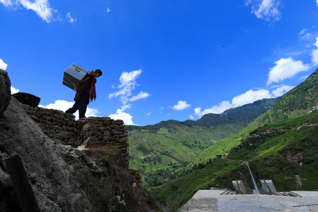 A silhouette of a woman with a large box on her back on top of a mountain on a beautiful day.