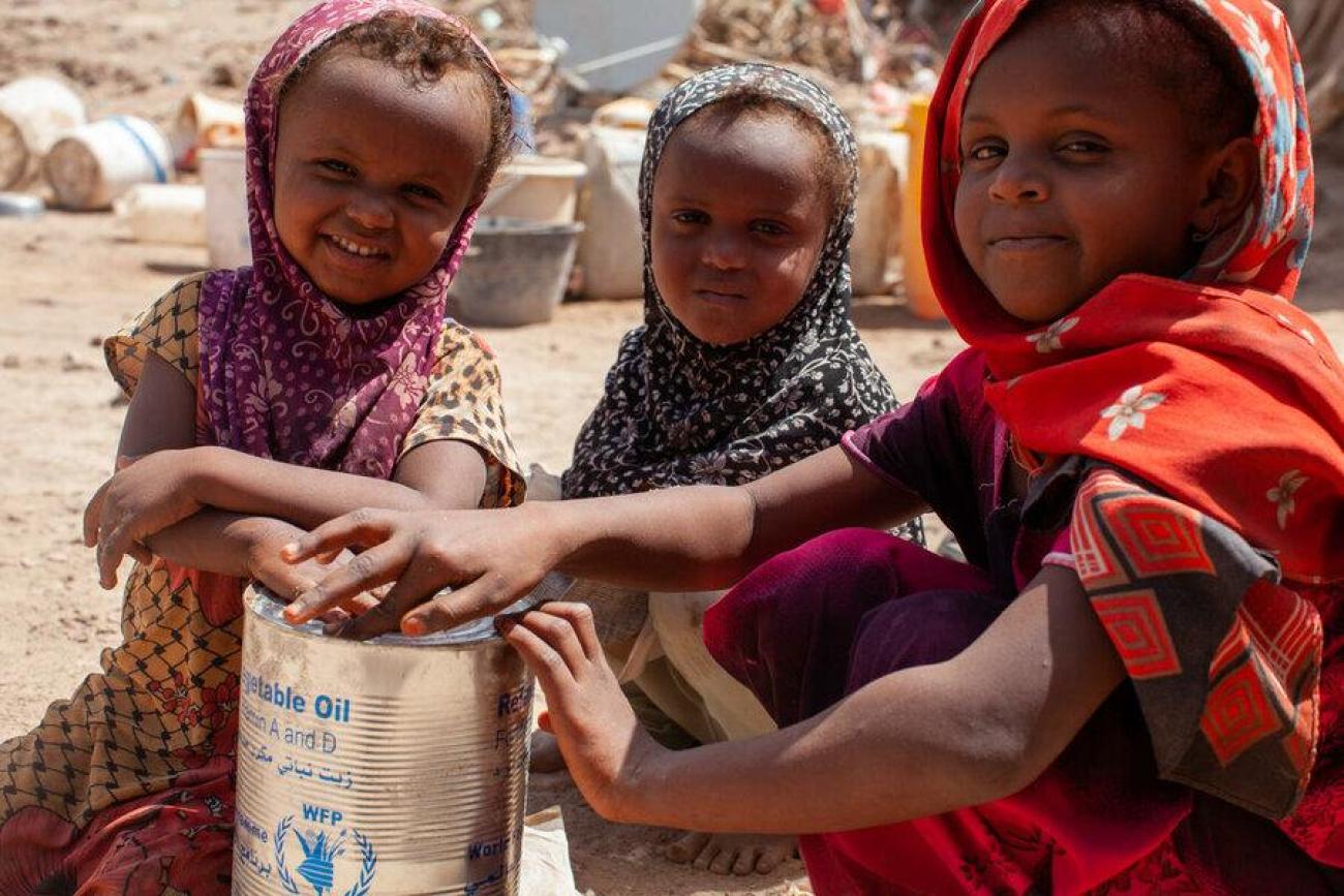 Three young girls sit and smile in front of a dusty background. 