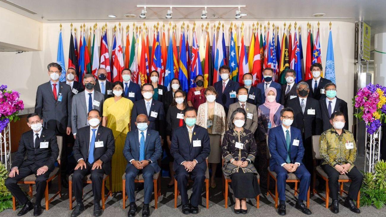 Un grupo de funcionarios posa para una foto, con banderas multicolores detrás de ellos.