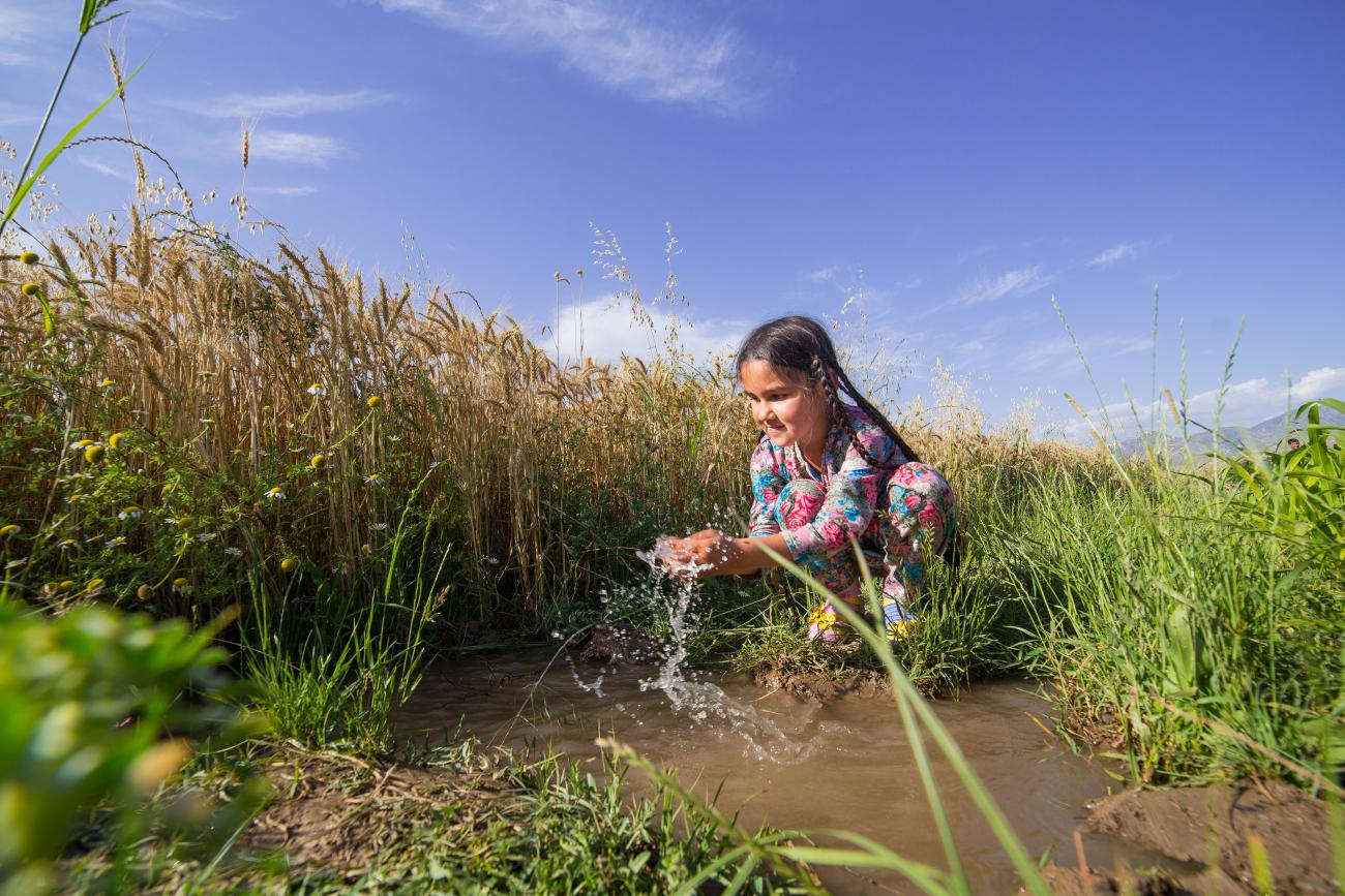 Au Tadjikistan, une petite fille aux cheveux tressés se lave les mains dans un ruisseau.