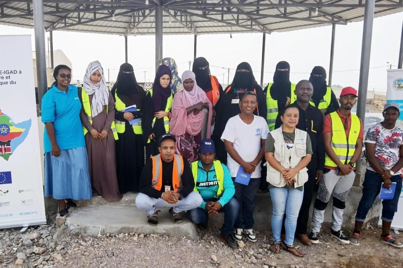 Un groupe d’hommes et de femmes, dont certaines portent un voile intégral noir, se tiennent côte à côte, en extérieur, et regardent en direction de la caméra en souriant.