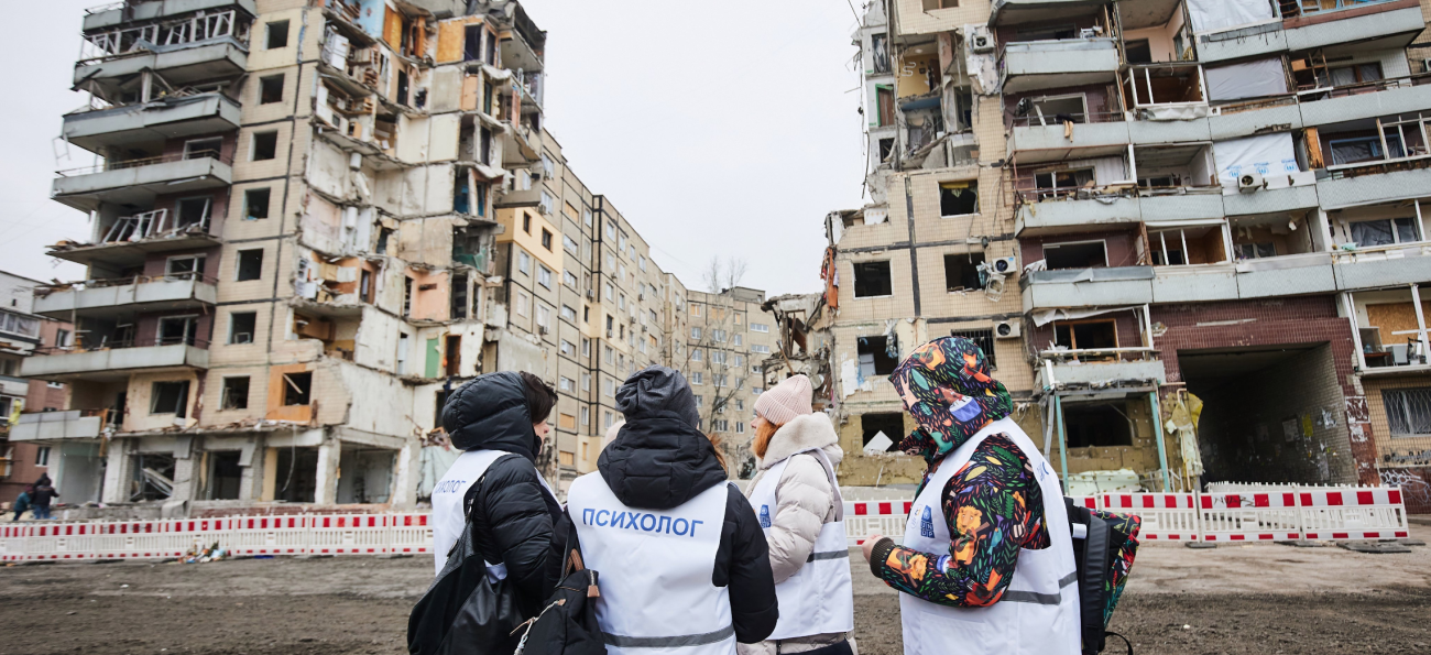 A small group stand before buildings that appear to have been bombed or destroyed.