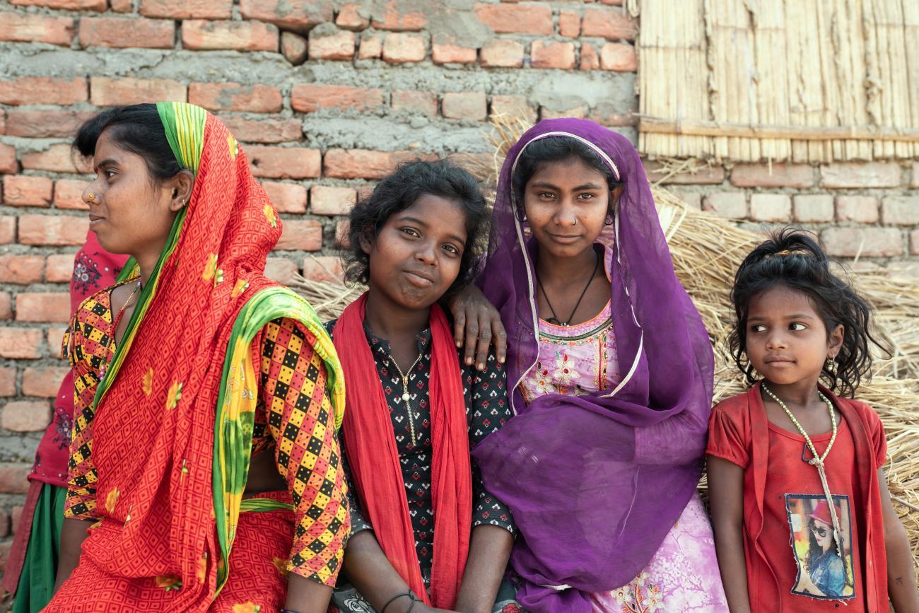 A group of girls in colorful outfits from Nepal huddle together and smile. 